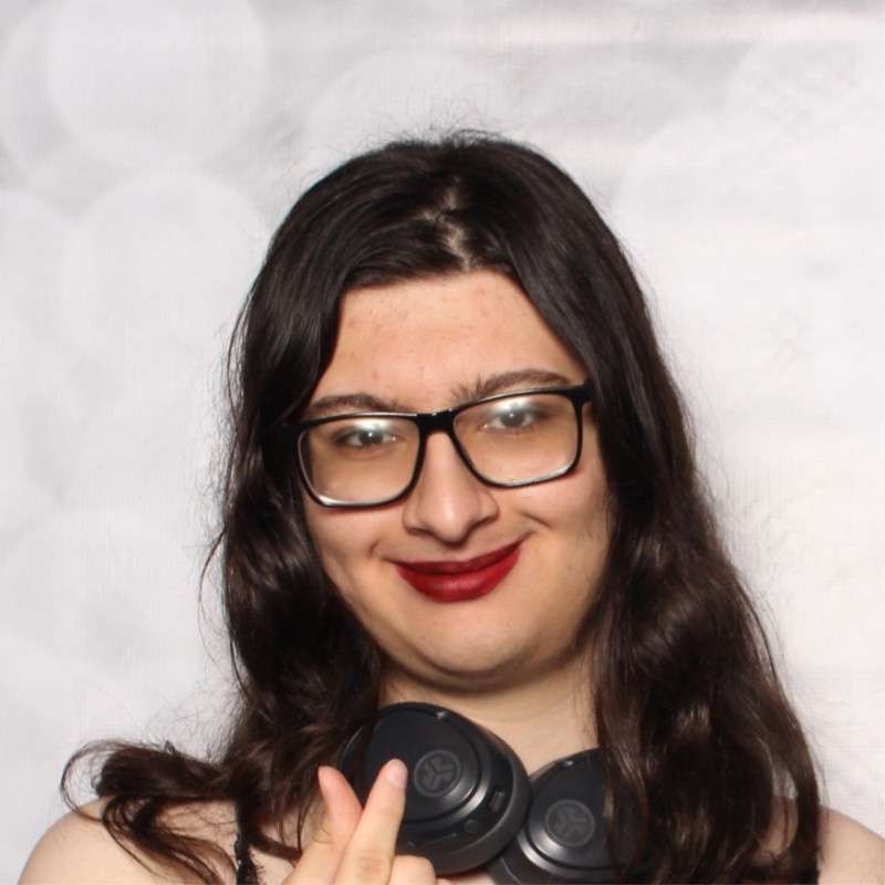 Picture of Feli Hoyos. A woman with long, wavy, brown hair and glasses is pictured smiling